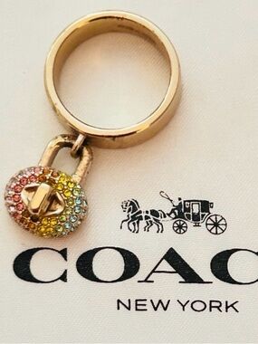 Coach Pavé Turnlock Ring, a gold-tone band ring with a dangling turnlock charm